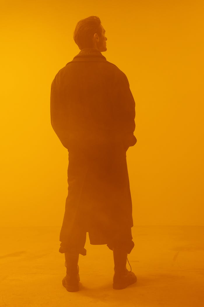 About Conceptual cyberpunk image of man in black coat against orange background.